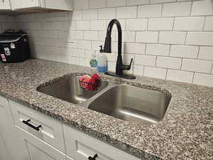 Details with dark stone counters, white cabinets, a sink, and backsplash