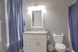 Full bathroom with toilet, a shower with shower curtain, vanity, and baseboards