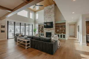 Living room featuring light wood-style floors, beam ceiling, a stone fireplace, and baseboards