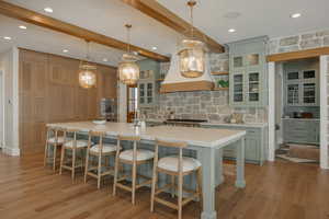 Kitchen featuring a spacious island, glass insert cabinets, decorative light fixtures, custom exhaust hood, and light countertops