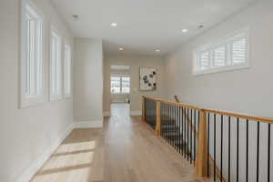 Hallway featuring baseboards, visible vents, an upstairs landing, light wood-type flooring, and recessed lighting