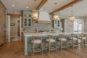 Kitchen featuring beam ceiling, a large island, light countertops, glass insert cabinets, and premium range hood