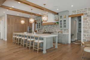 Kitchen featuring glass insert cabinets, decorative light fixtures, light countertops, custom exhaust hood, and a large island with sink