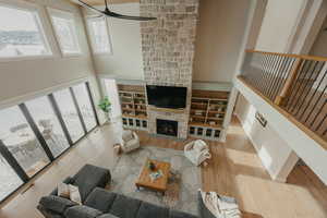 Living area with stairs, a stone fireplace, light wood-type flooring, and a high ceiling