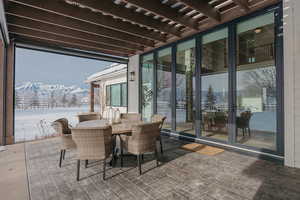 Snow covered patio with a mountain view, outdoor dining area, and a pergola