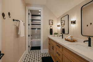 Bathroom featuring lofted ceiling, a sink, baseboards, and double vanity