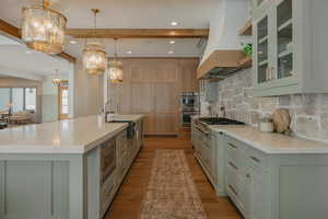 Kitchen with glass insert cabinets, a sink, custom exhaust hood, a large island with sink, and pendant lighting