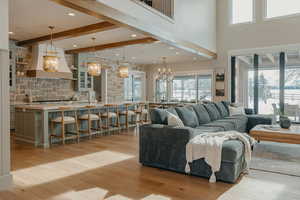 Living area with light wood-type flooring, beam ceiling, a notable chandelier, and a towering ceiling