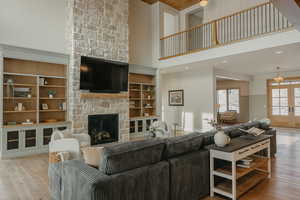 Living room with light wood finished floors, wainscoting, french doors, and a stone fireplace