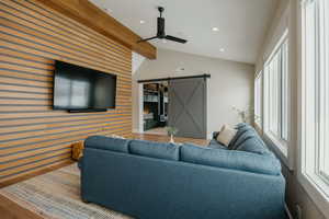 Living room with vaulted ceiling with beams, a barn door, recessed lighting, an accent wall, and wood finished floors