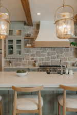 Kitchen featuring pendant lighting, light countertops, custom range hood, glass insert cabinets, and a kitchen bar