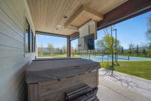 View of patio / terrace with a tennis court, a hot tub, and fence