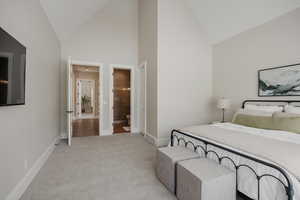 Bedroom with high vaulted ceiling, light colored carpet, connected bathroom, and baseboards