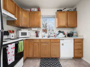 Kitchen featuring an extra window due to being an end unit, light countertops, brown cabinetry, a sink, white appliances, and under cabinet range hood