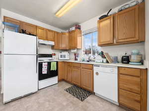 Kitchen featuring extra windows, due to being an end unit, light countertops, brown cabinetry, a sink, white appliances, and under cabinet range hood