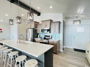 Kitchen featuring light stone counters, appliances with stainless steel finishes, a breakfast bar, hanging light fixtures, and a sink