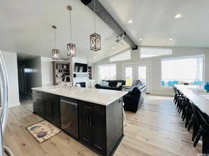 Kitchen with dishwasher, an island with sink, open floor plan, light countertops, and dark cabinetry