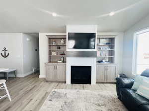Living room featuring a fireplace, visible vents, light wood-style flooring, a textured ceiling, and baseboards