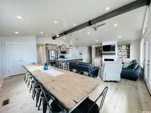 Dining area featuring lofted ceiling with beams, light wood finished floors, a fireplace, and visible vents