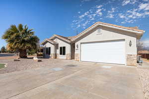 View of front of house with solar panels, stucco siding, a garage, stone siding, and driveway