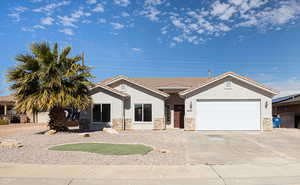 View of front facade featuring an attached garage, stone siding, driveway, and stucco siding