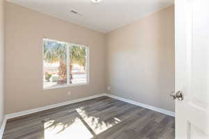 Empty room featuring dark wood-style flooring, visible vents, and baseboards