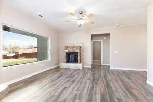 Unfurnished living room with a fireplace, wood finished floors, a ceiling fan, visible vents, and baseboards