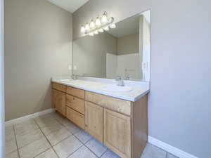 Full bath featuring double vanity, tile patterned flooring, a sink, and baseboards