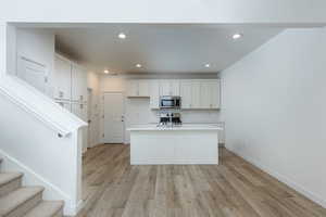 Kitchen featuring a center island with sink, white cabinets, light wood-style flooring, appliances with stainless steel finishes, and light countertops