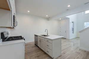 Kitchen with a sink, white cabinets, light countertops, appliances with stainless steel finishes, and an island with sink