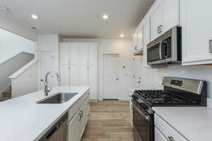 Kitchen featuring light wood-style flooring, appliances with stainless steel finishes, white cabinets, and a sink