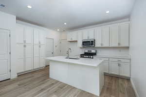 Kitchen featuring a kitchen island with sink, a sink, white cabinetry, light countertops, and appliances with stainless steel finishes
