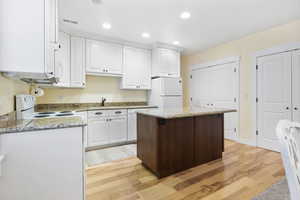 Kitchen with white appliances, a sink, white cabinetry, and a center island