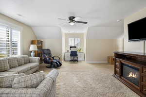 Living room featuring light carpet, baseboards, visible vents, a glass covered fireplace, and lofted ceiling