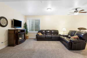 Living room with a glass covered fireplace, light carpet, ceiling fan, and baseboards