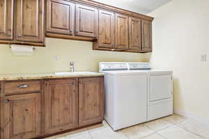 Washroom featuring cabinet space, light tile patterned floors, baseboards, washer and dryer, and a sink