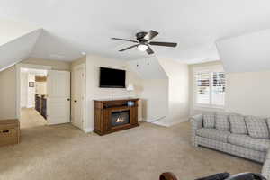 Living room with light carpet, baseboards, a ceiling fan, a glass covered fireplace, and lofted ceiling