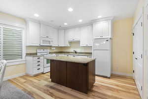 Kitchen featuring light stone countertops, white appliances, light wood-style flooring, and white cabinetry