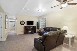 Living room featuring ceiling fan, baseboards, light colored carpet, and a glass covered fireplace