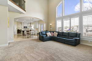 Living room featuring arched walkways, a notable chandelier, a towering ceiling, light carpet, and baseboards