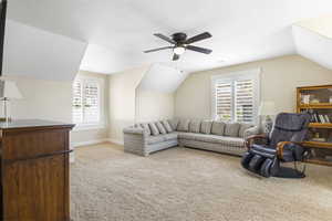 Living room featuring lofted ceiling, ceiling fan, baseboards, and light colored carpet