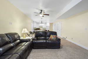 Living room featuring baseboards, ceiling fan with notable chandelier, visible vents, and light colored carpet