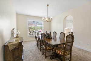 Dining area with light carpet, a chandelier, arched walkways, and baseboards