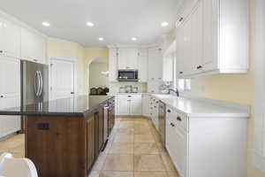 Kitchen featuring arched walkways, recessed lighting, appliances with stainless steel finishes, white cabinetry, and a kitchen island