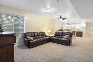 Living room featuring ceiling fan with notable chandelier, baseboards, and light colored carpet