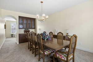 Dining space featuring light carpet, baseboards, arched walkways, and a notable chandelier