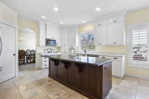 Kitchen with arched walkways, white cabinets, a kitchen island, stainless steel microwave, and a breakfast bar