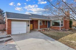 Single story home featuring brick siding, a shingled roof, concrete driveway, a garage, and a front lawn