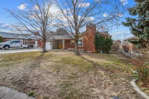 View of front of house featuring brick siding, fence, concrete driveway, a chimney, and a front yard