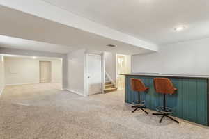 Bar with light colored carpet, visible vents, a bar, baseboards, and stairs